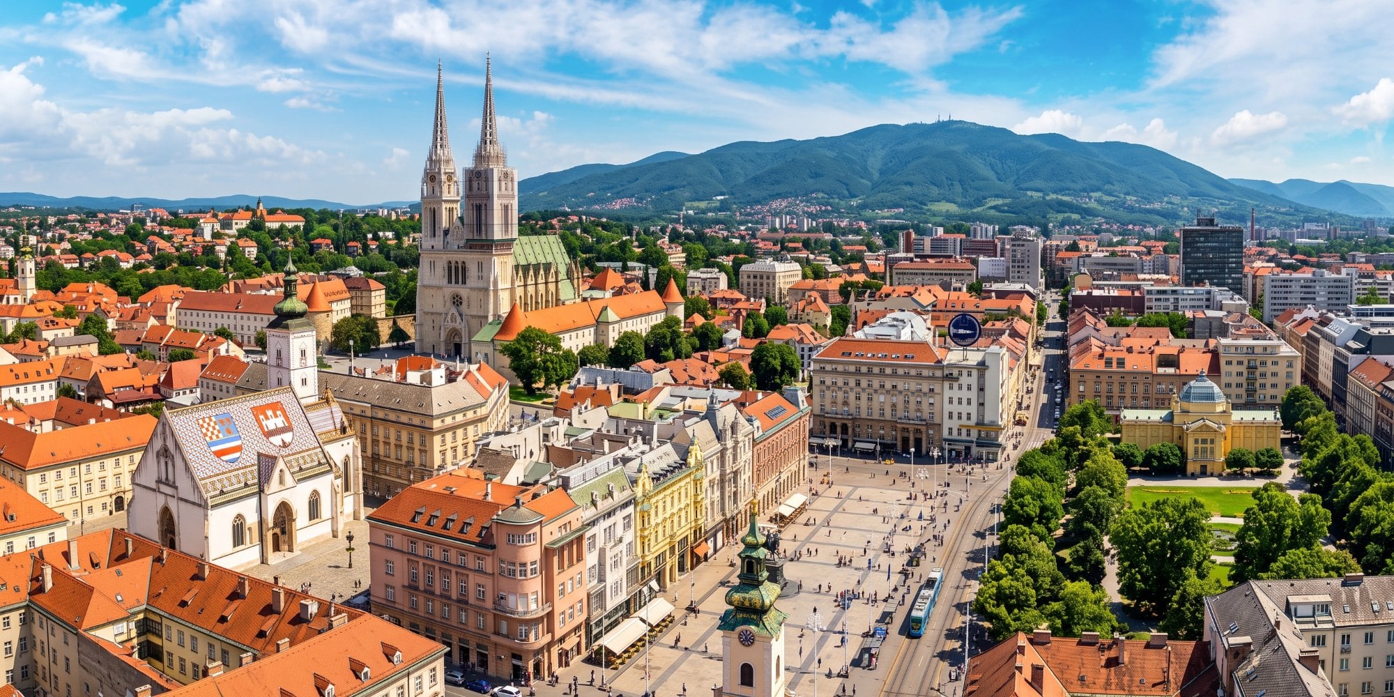 Panoramski pogled iz zraka na sunčani Zagreb s Trgom bana Jelačića, Zagrebačkom katedralom, crkvom sv. Marka i planinom Medvednicom u pozadini.